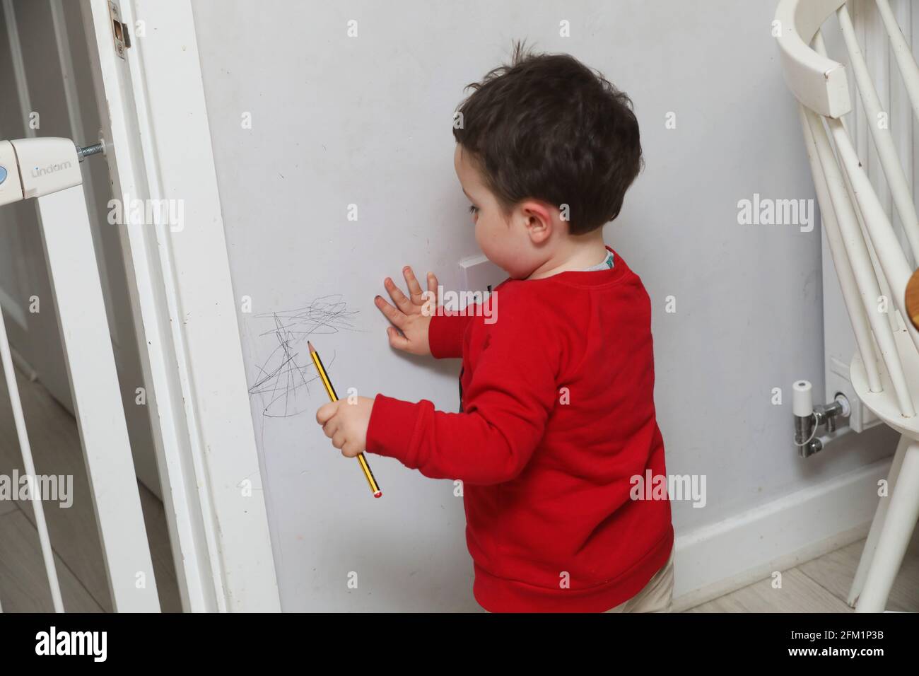 A young boy pictured drawing on the walls with a pencil in West Sussex, UK. Stock Photo