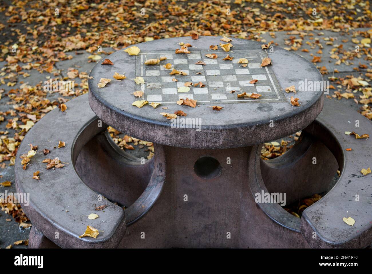 An empty chessboard on a concrete table outiside in a park in the Autumn, empty of people, close-up and side view, emtpy city in the pandemics concept Stock Photo