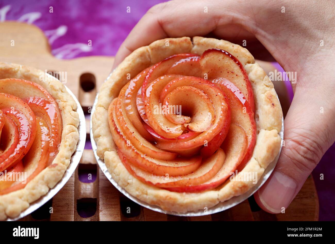 Man's hands placing a fresh baked delectable mini apple rose tartlet on the wooden breadboard Stock Photo