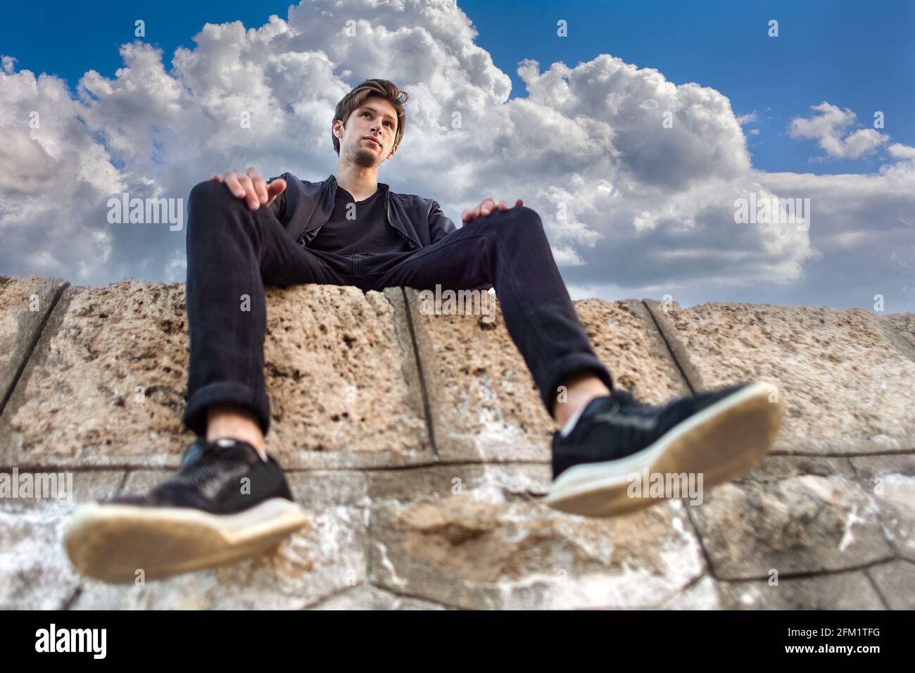 Bottom view of young man in his 20s sitting on stones of pier. Stock Photo