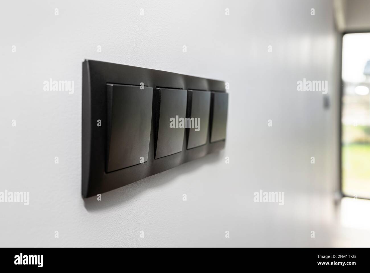 Black frame with a four-button light switch on the gray wall of the house. Stock Photo