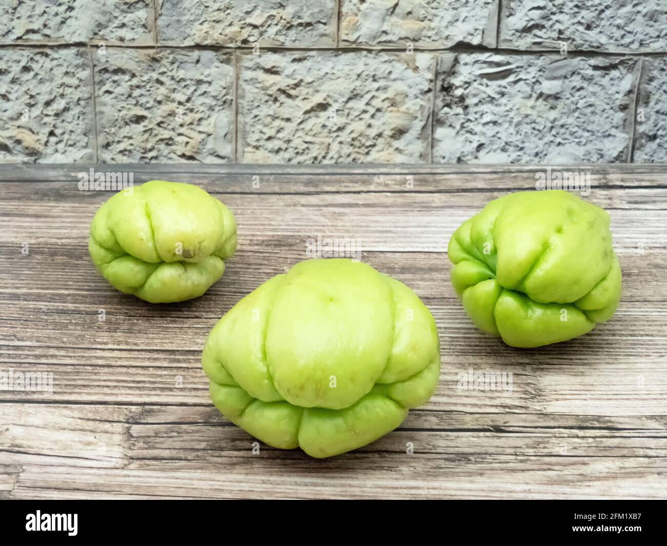 Three fruits of chayote on wood in front of a wall Stock Photo