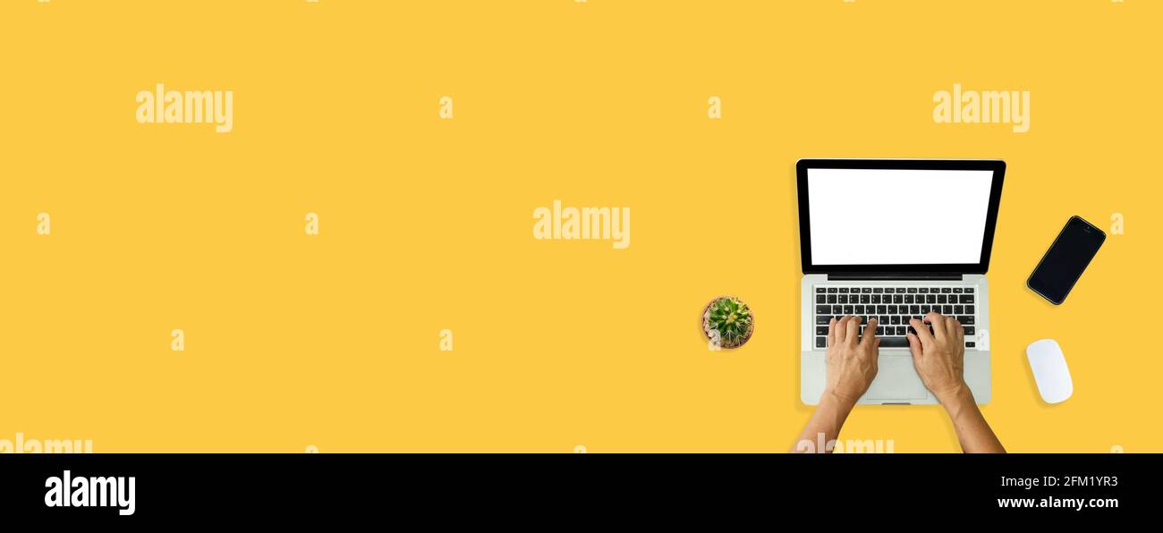 Hand using computer laptop and mouse, phone from above on yellow background. Stock Photo