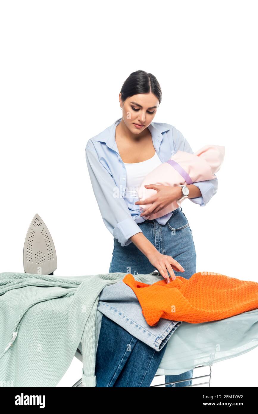 young mother holding newborn baby near clothes on ironing board ...