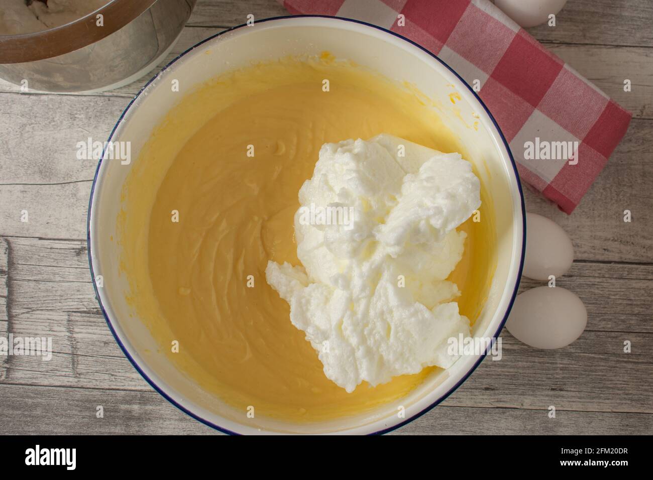 Fresh stirred cake batter with whipped egg white in a bowl on rustic wooden table background. Overhead view Stock Photo