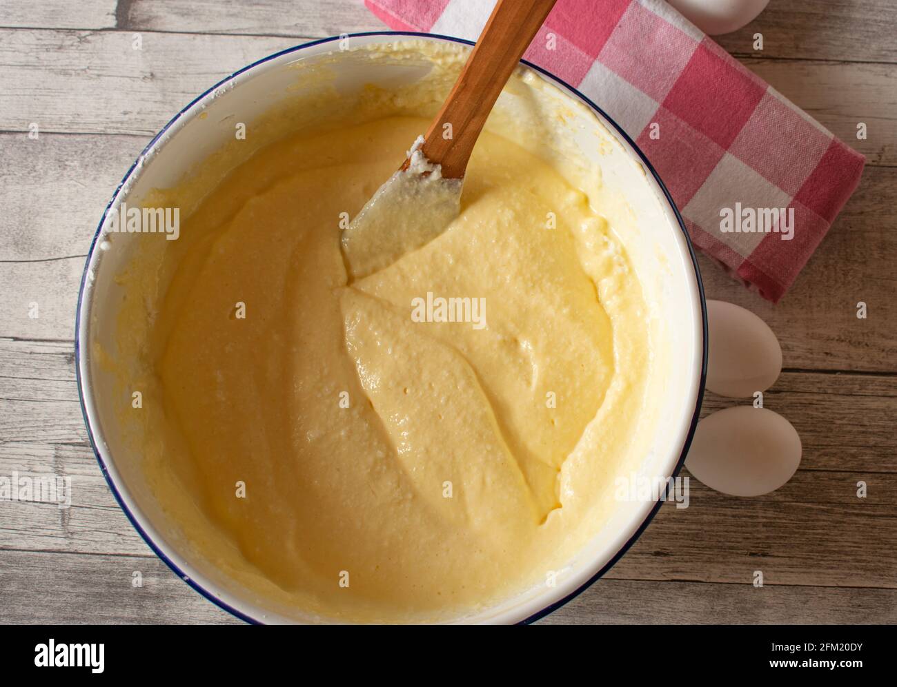 cake batter with fresh whipped egg white in a white enamel bowl on wooden table background Stock Photo
