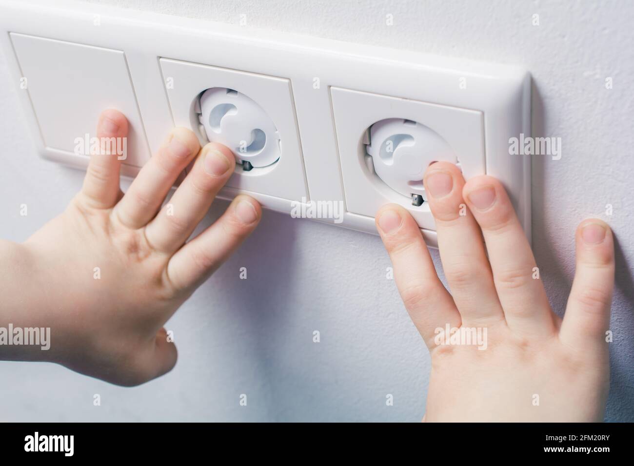 Two Child Hands Touching Wall Socket With Safety Plugs Prevent Child