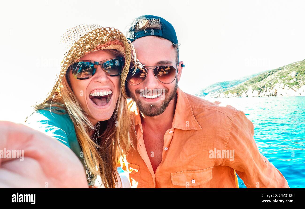 Young happy couple in love taking selfie at sailboat excursion with water camera - Boat trip life style in exotic scenarios - Youth lifestyle Stock Photo