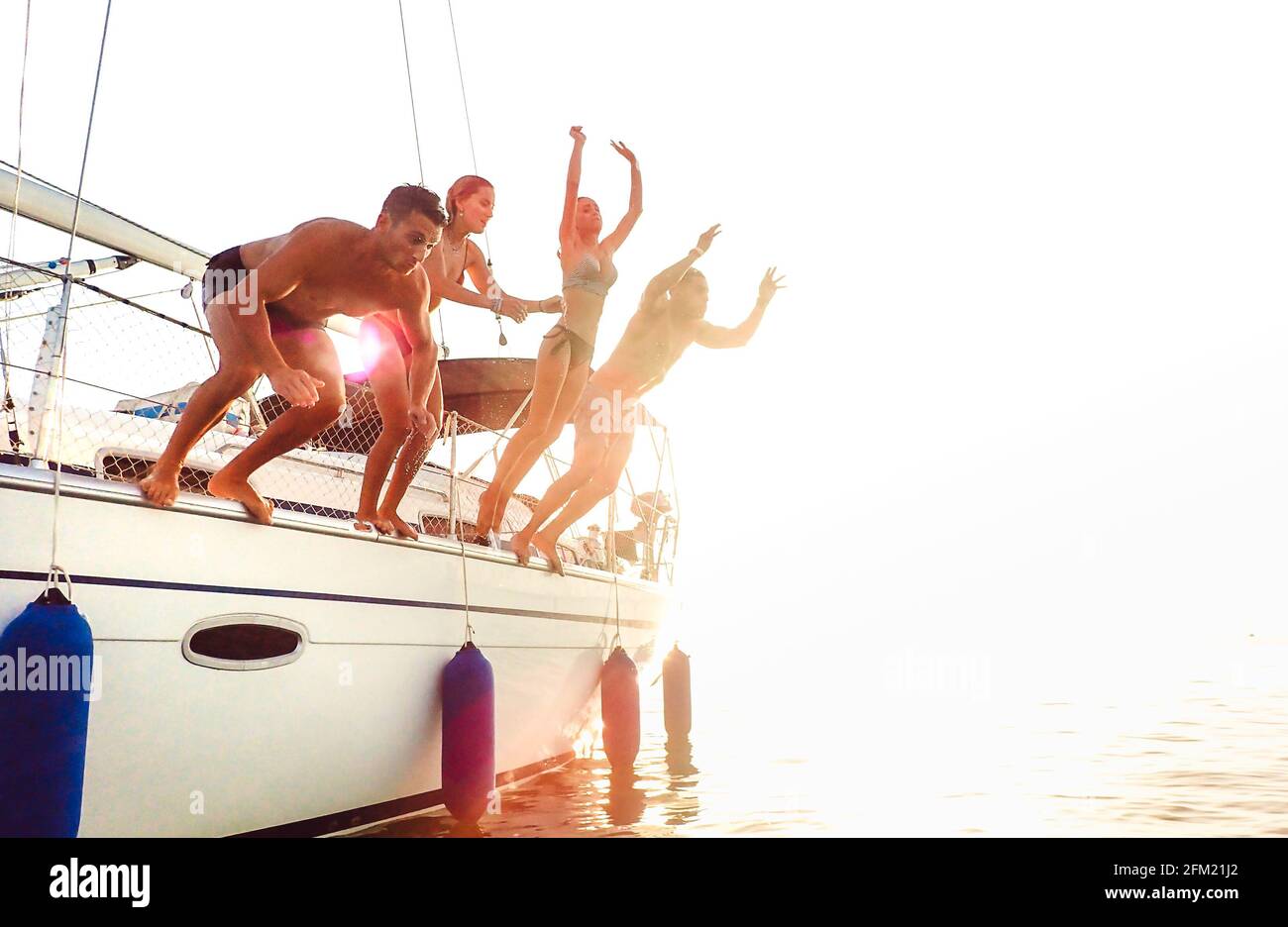 Side view of young crazy friends jumping from sailboat on sea ocean trip - Men and women having summer fun together at sail boat party day - Luxury ex Stock Photo
