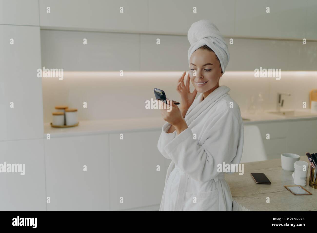 Happy healthy woman in bathrobe applying skin care product on face ...