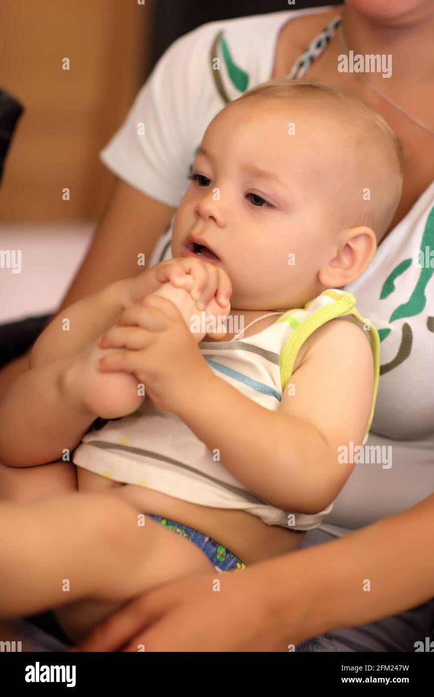 Baby boy pulls his foot on mother's lap Stock Photo - Alamy