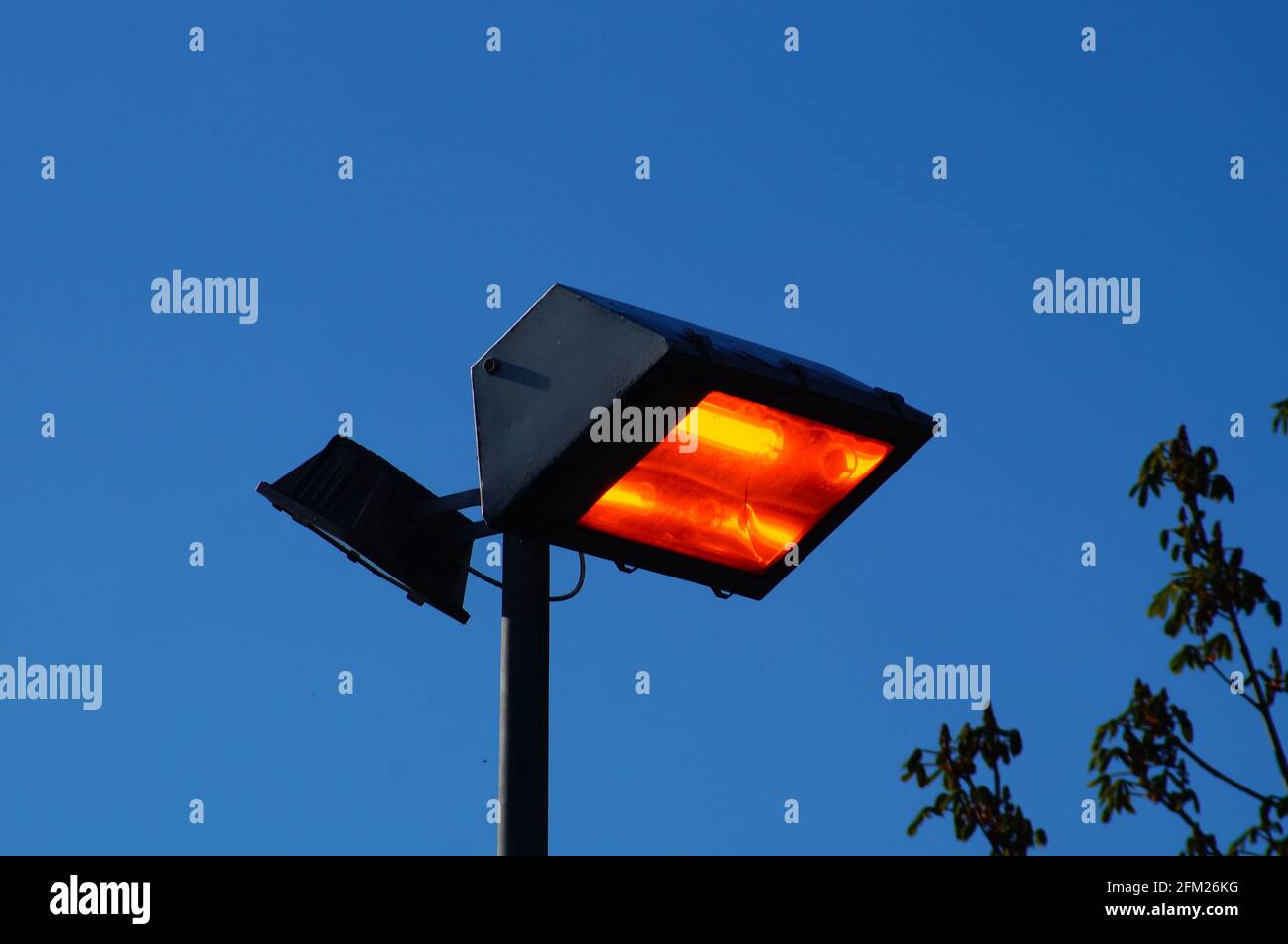 Waste of energy: A floodlight burns in bright sunlight. Stock Photo