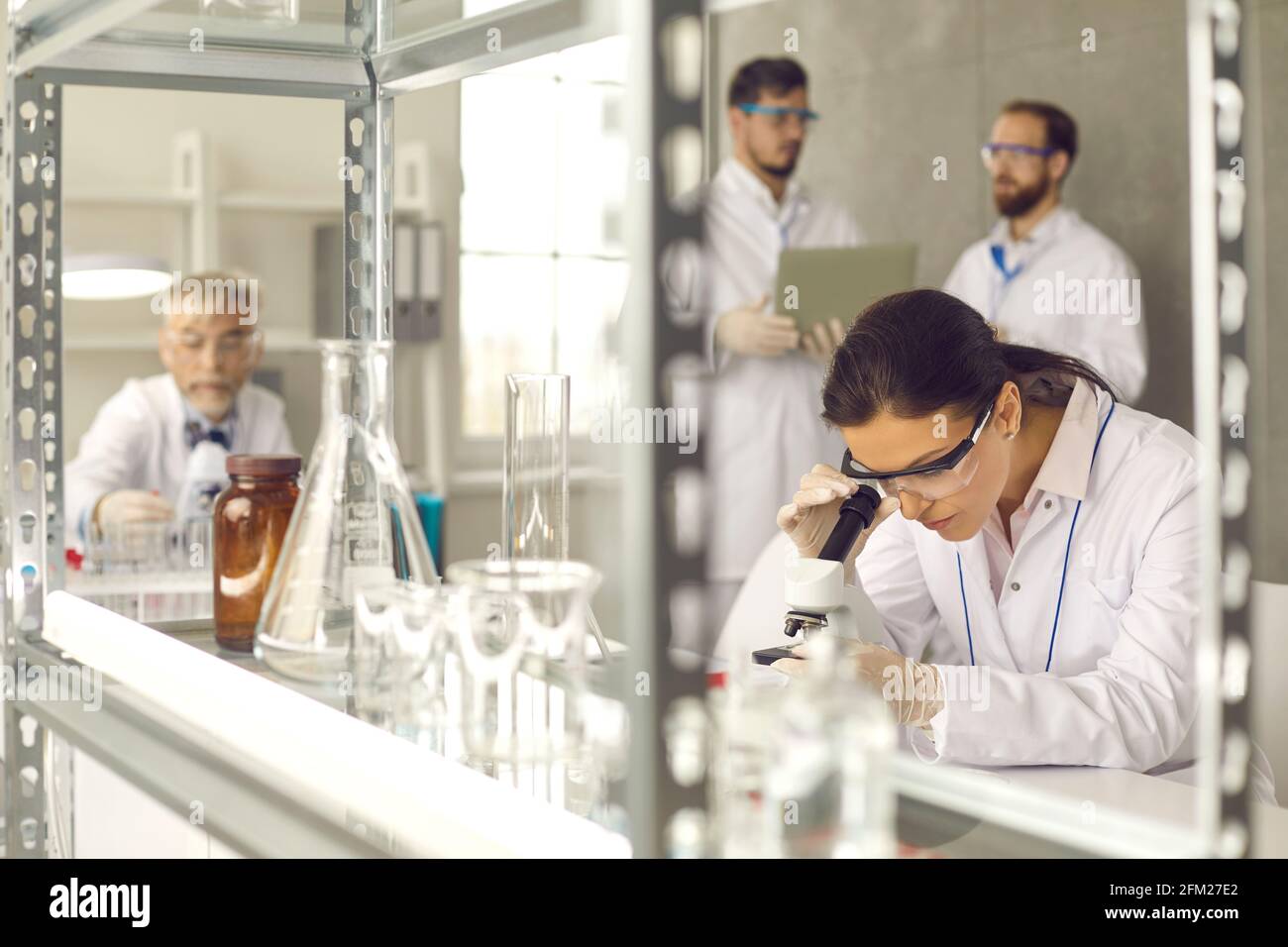 Focus on woman wearing safety goggles and lab coat working with microscope Stock Photo