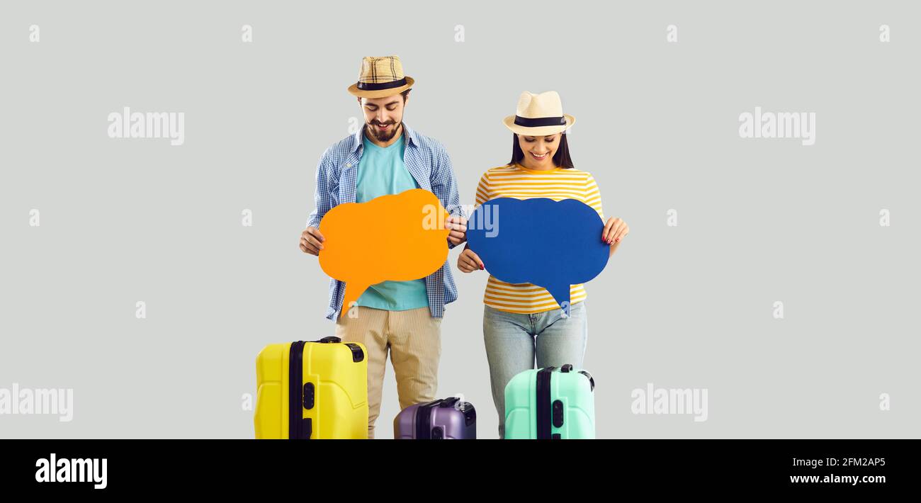 Two happy tourists with travel suitcases standing in studio holding conversation bubbles Stock Photo