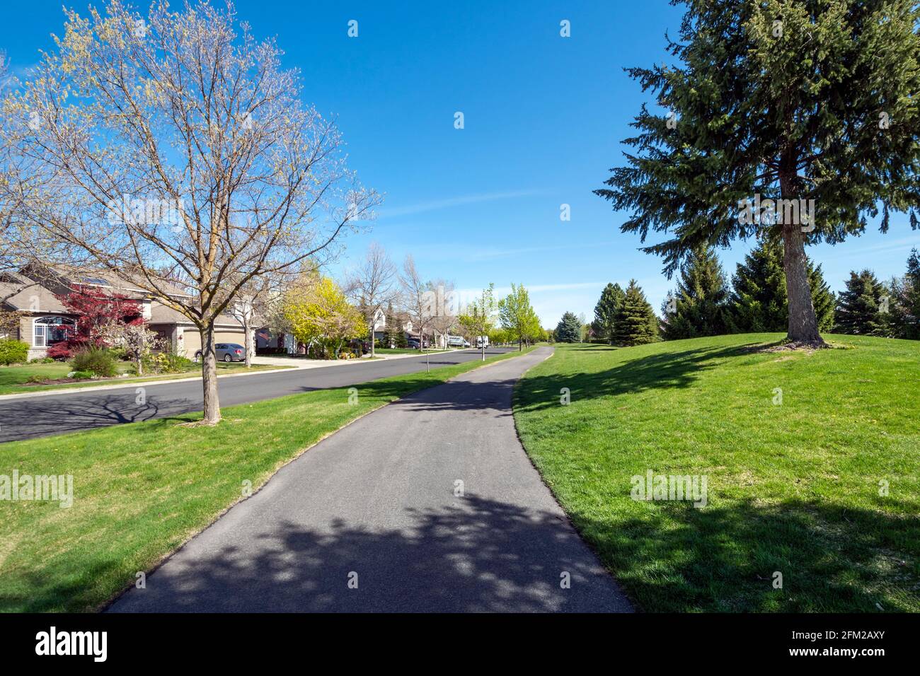 A suburban street of homes in a subdivision across from a park and walking trail path in the town of Coeur d'Alene, Idaho, USA Stock Photo