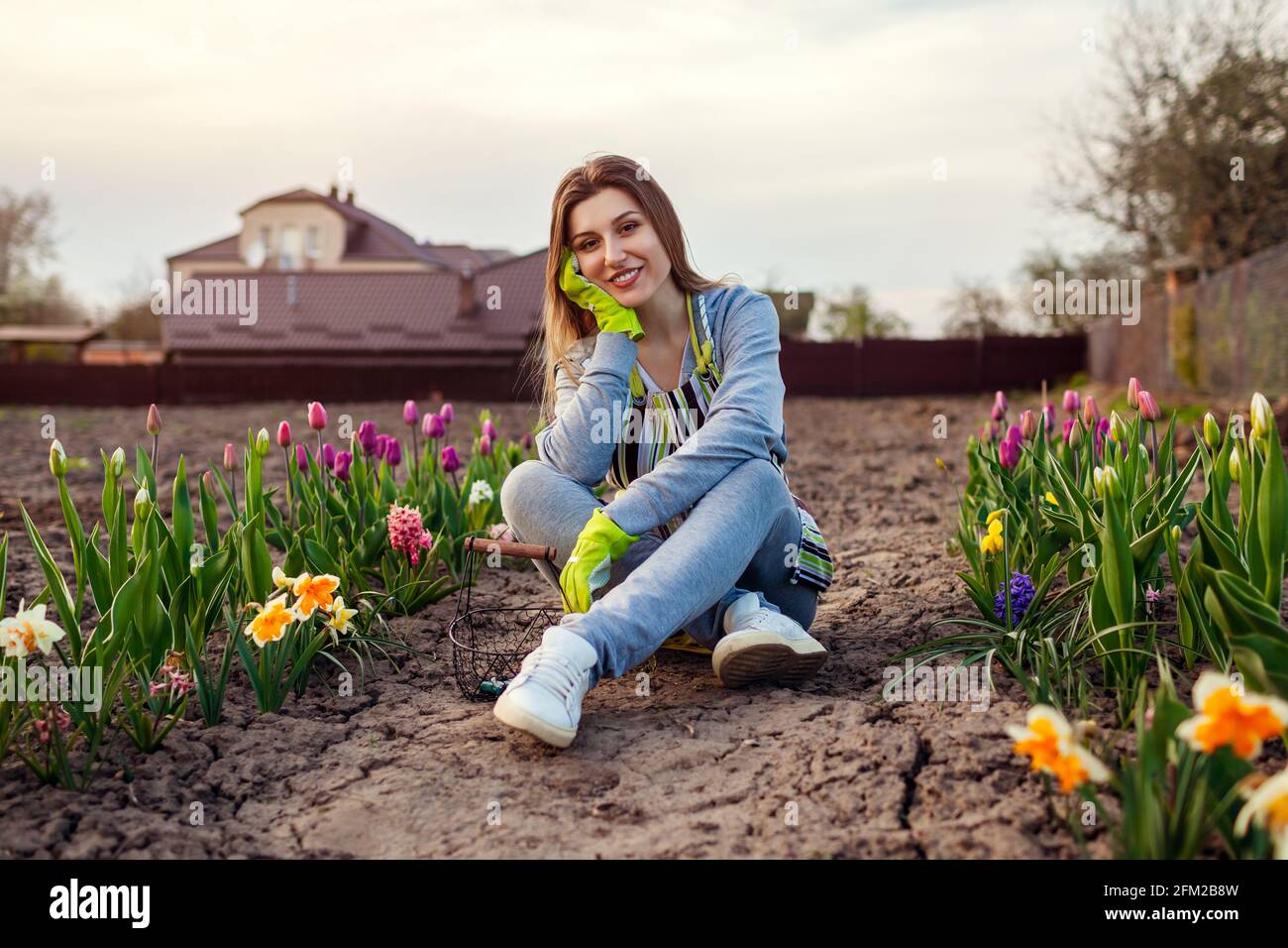 Gardener relaxing among fresh tulips, daffodils, hyacinths in spring garden. Happy woman enjoys colorful flowers Stock Photo
