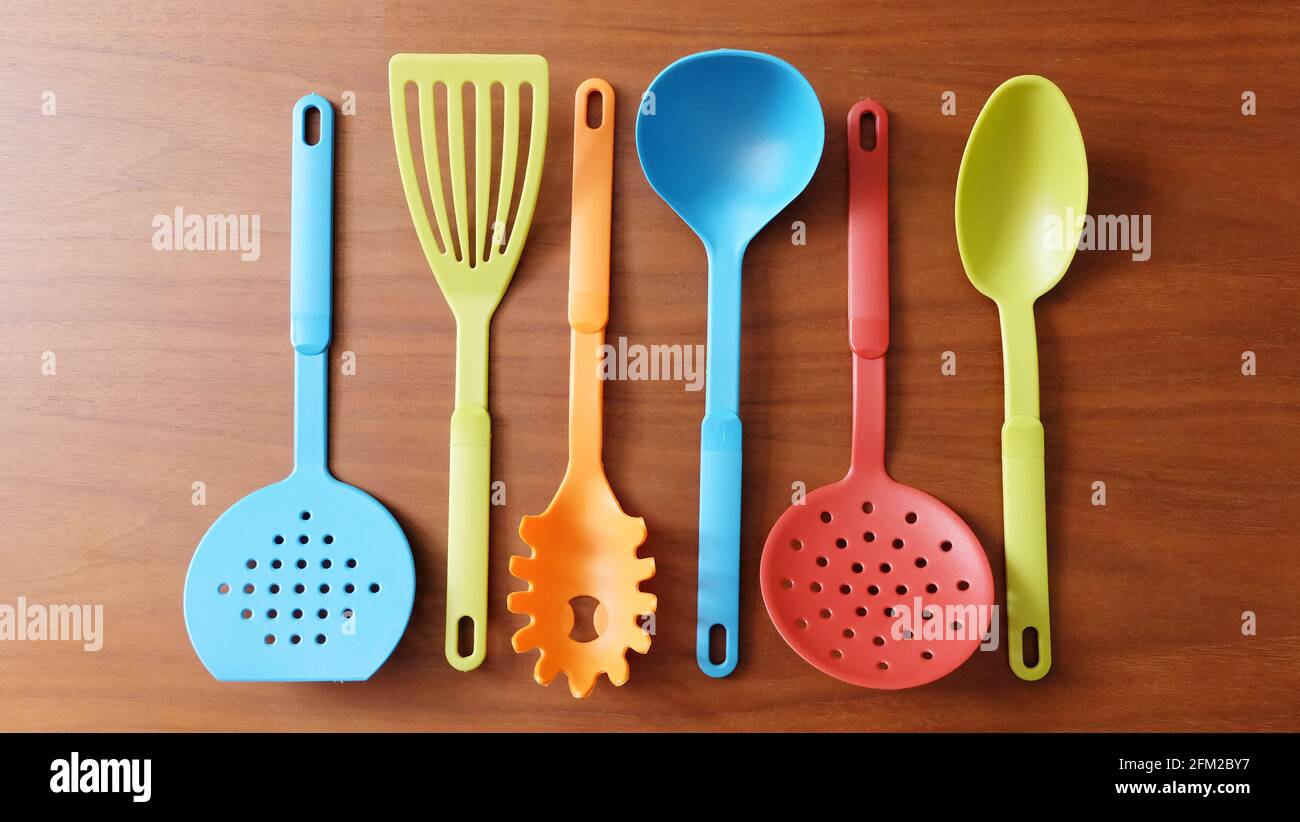 A variety of colorful kitchen utensils arranged neatly side by side on a wooden surface. Stock Photo