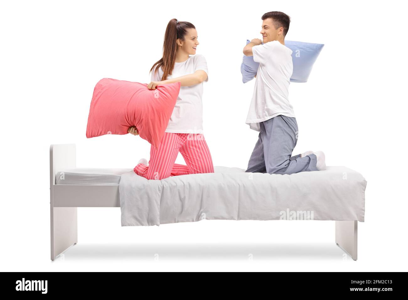 Young man and woman in pajamas fighting with pillows on a bed isolated on white background Stock Photo