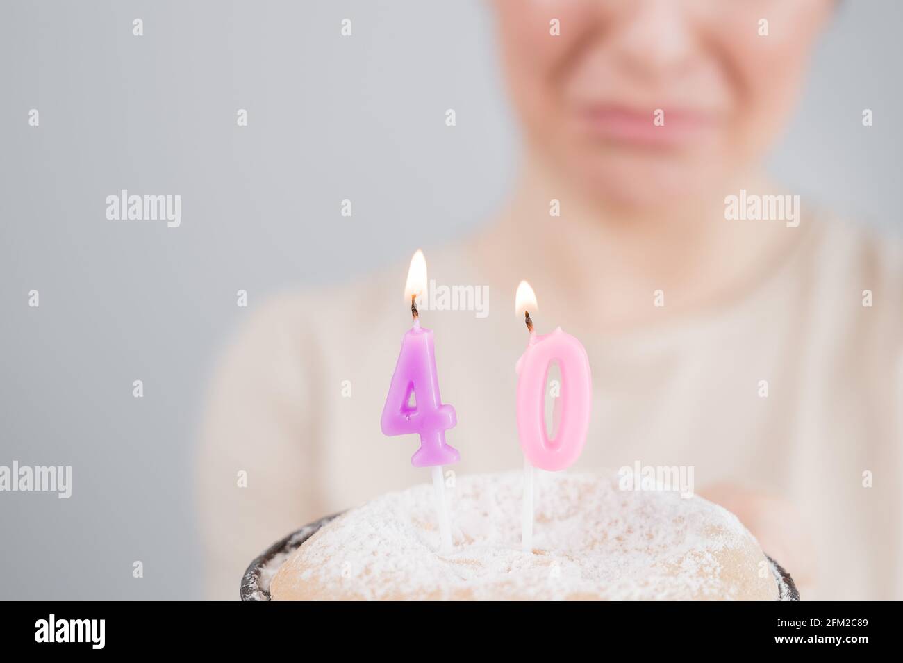 Unhappy woman holding a cake with candles for her 40th birthday. The girl cries about the loss of youth. Stock Photo