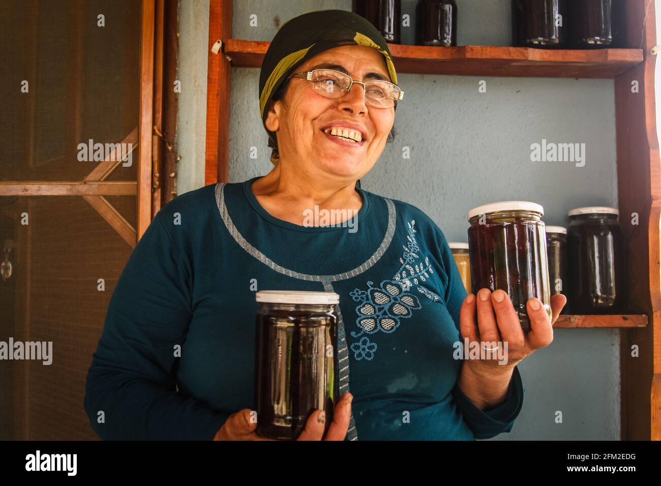 Gokceada, Canakkale - Turkey - May 07 2013: A turkish female farmer holding two jars of jam in her hands and smiling, Tepekoy Stock Photo