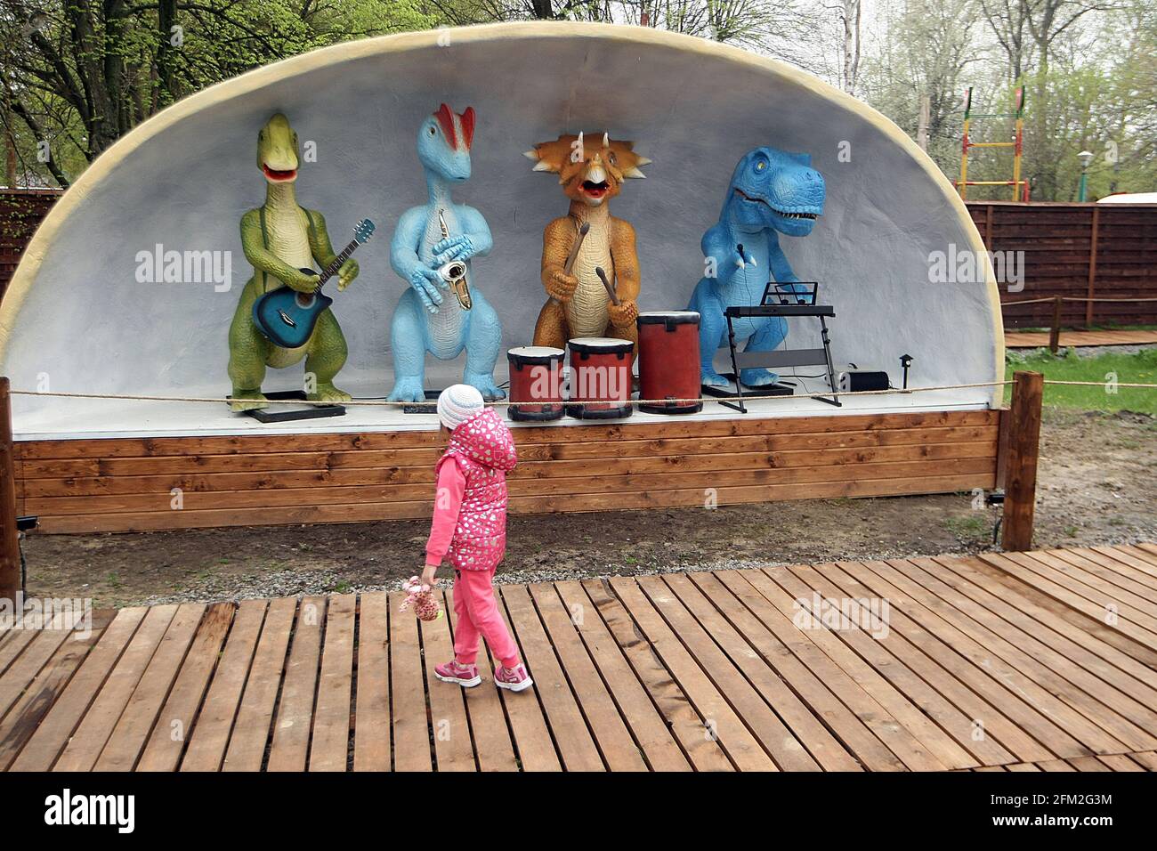 KYIV, UKRAINE - MAY 02, 2021 - A girl passes by the Music Band installation of robotic dinosaur figures on the territory of the metropolitan Hydropark Stock Photo
