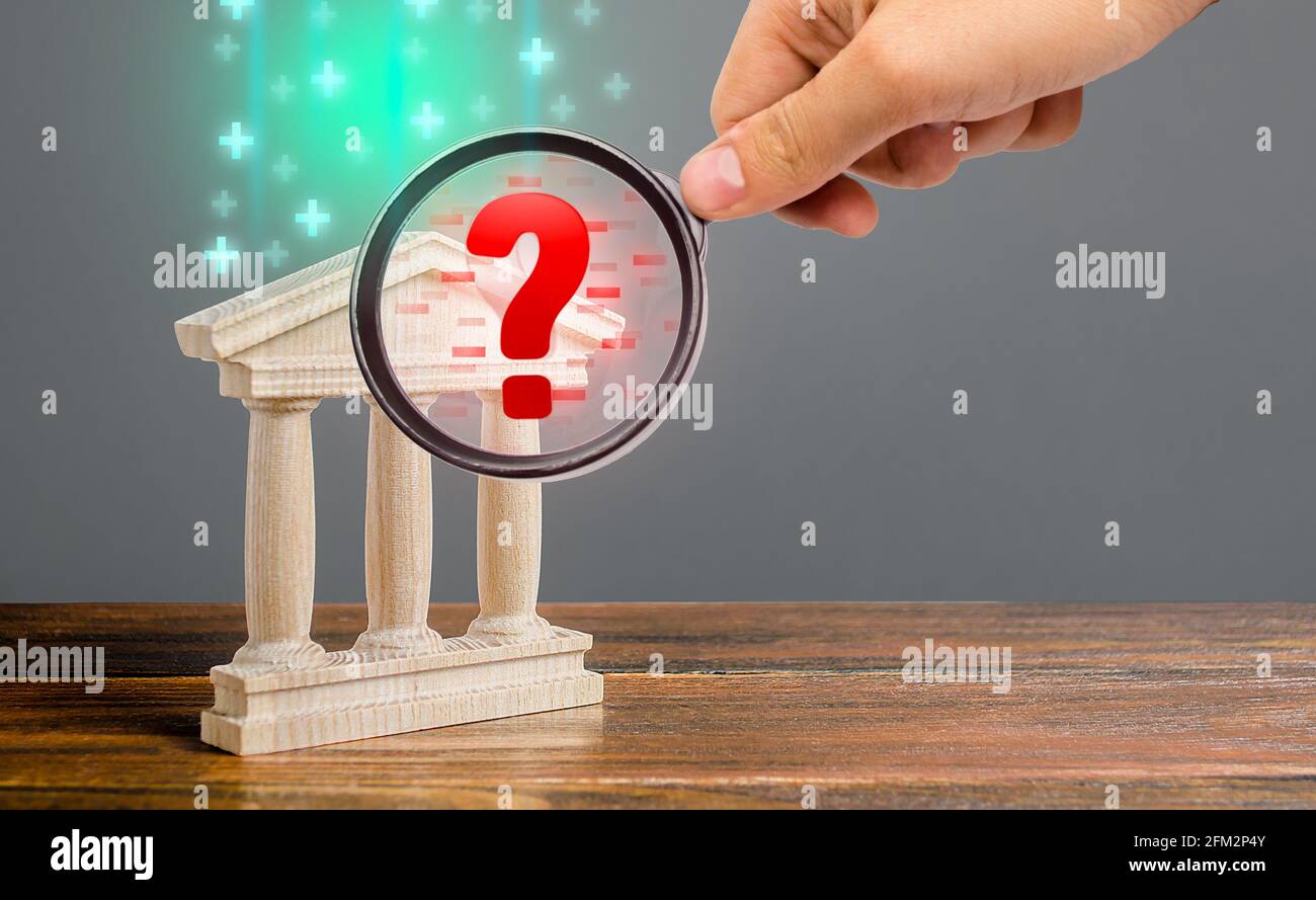 A hand with a magnifying glass inspects bank and finds financial violations. Audit and accounting. Money laundering, sanctions evasion. Insolvency, mi Stock Photo