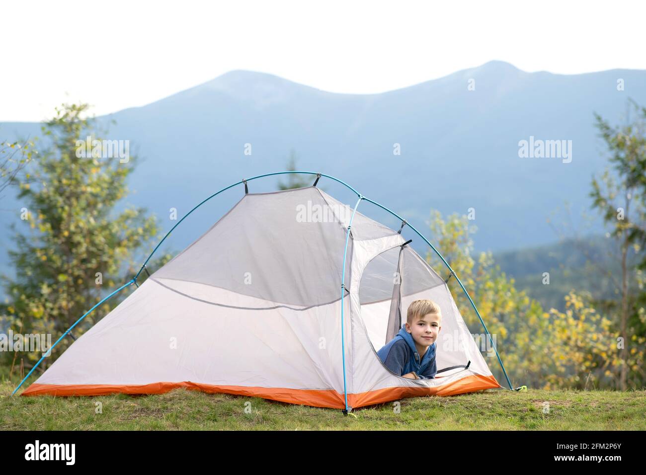 Happy child boy resting alone in a tourist tent at mountain campsite ...