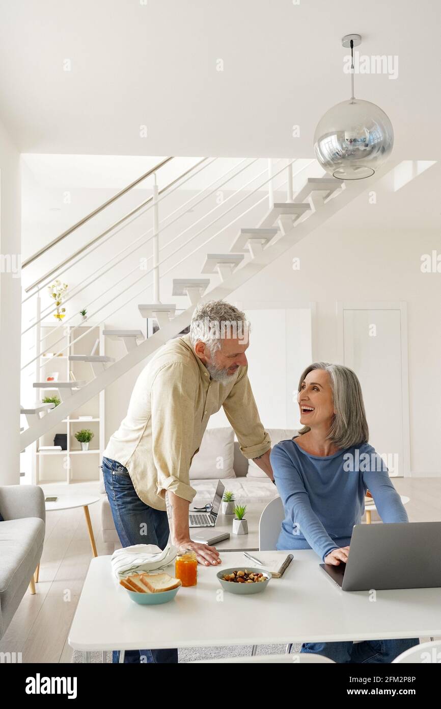 Happy middle aged couple using laptop computer and talking at home. Stock Photo