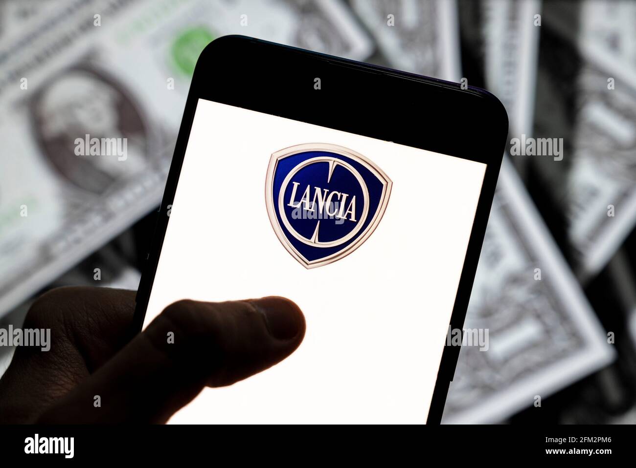 In this photo illustration the Italian automobile manufacturer Lancia logo seen displayed on a smartphone with USD (United States dollar) currency in the background. Stock Photo