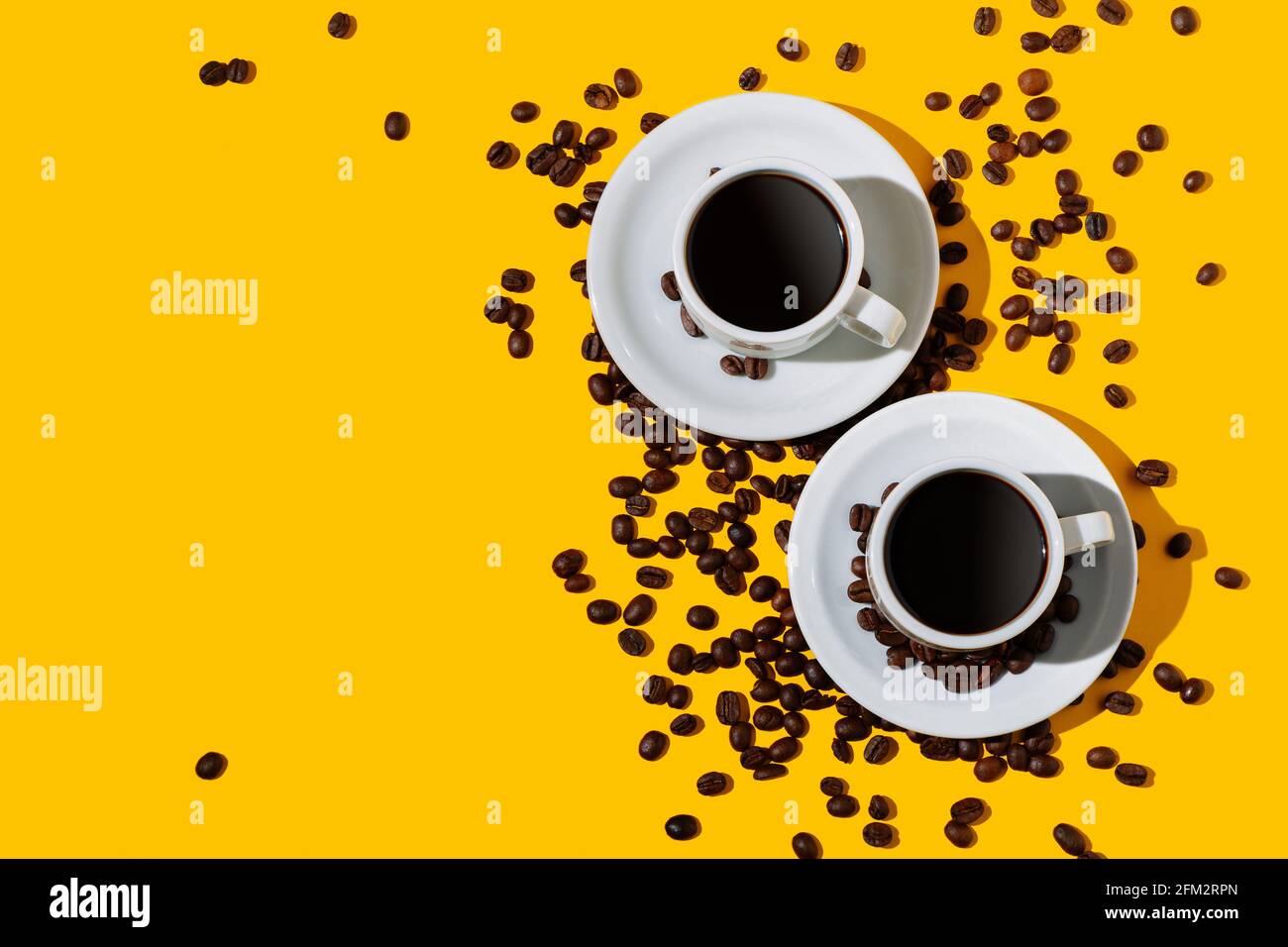 Top view of two coffee cup over a bright yellow color background and many beans spilled around. Stock Photo