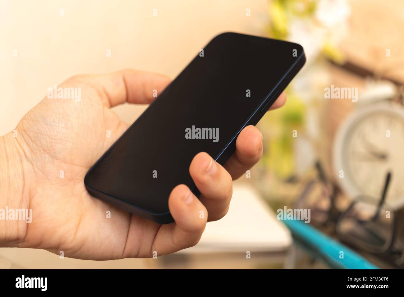 Man hold black smartphone on home interior background, concept of using mobile phone Stock Photo