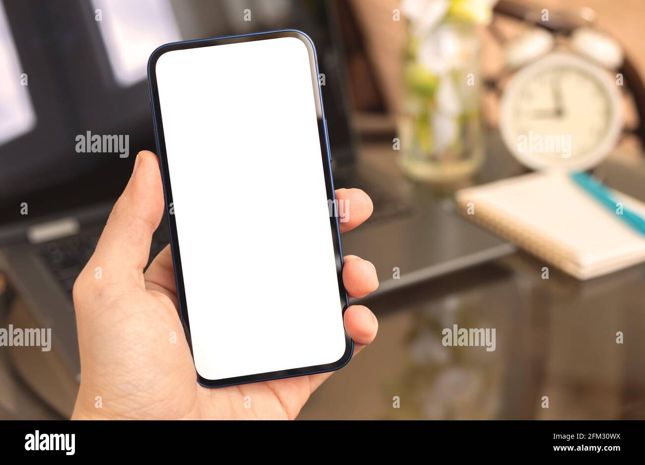 Man using smartphone mockup on background of laptop, home interior with alarm clock and homeplant, copy space Stock Photo
