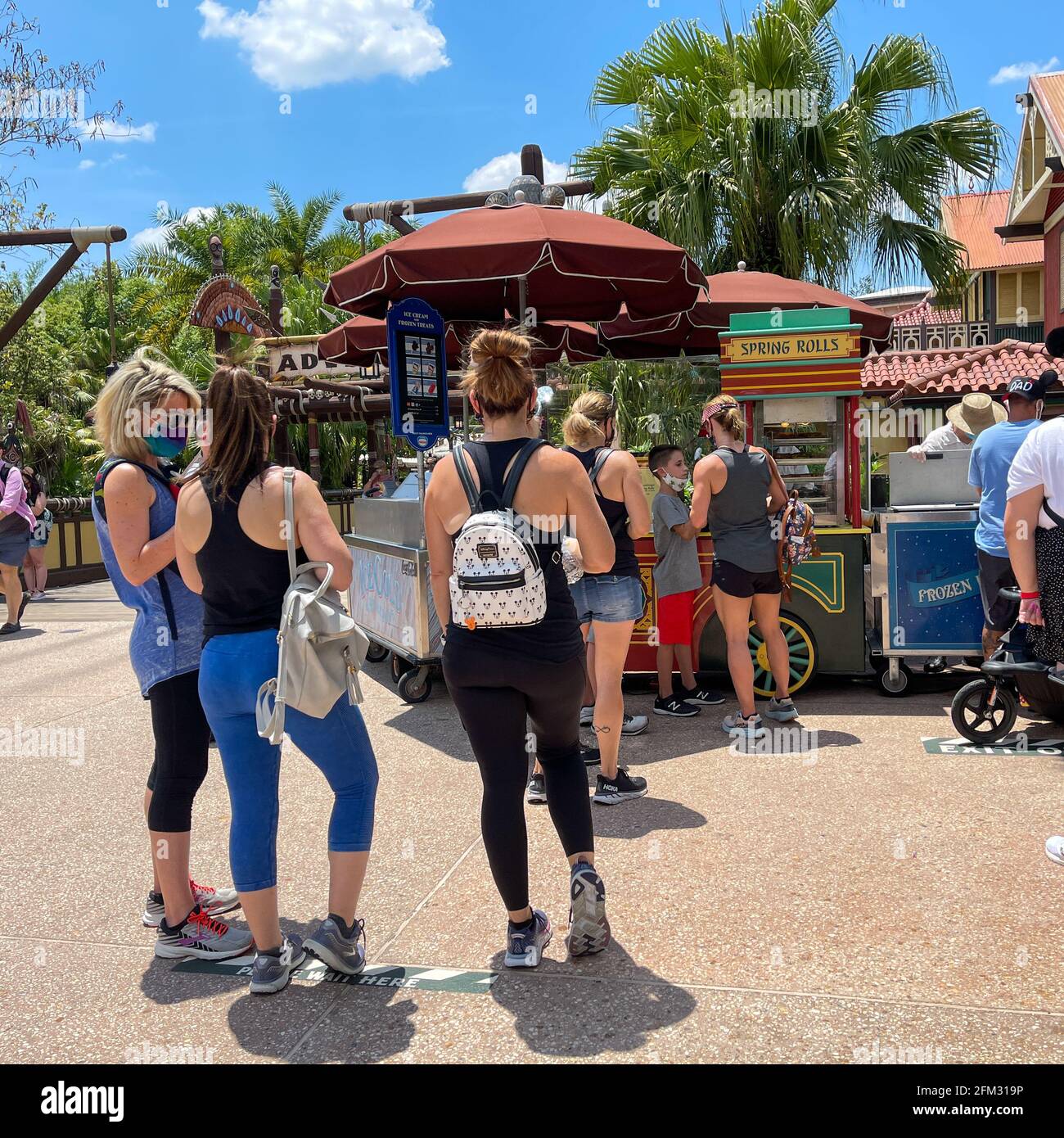Orlando, FL USA - May 2, 2021:  People waiting in line to buy Cheeseburger and Pepperoni Spring Rolls from a food cart at Disney World Magic Kingdom. Stock Photo