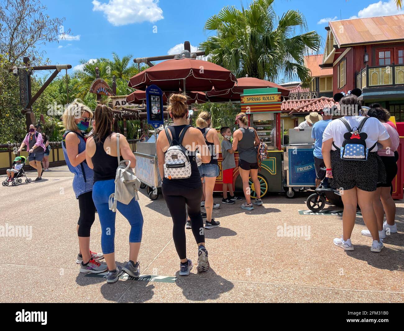 Orlando, FL USA - May 2, 2021:  People waiting in line to buy Cheeseburger and Pepperoni Spring Rolls from a food cart at Disney World Magic Kingdom. Stock Photo