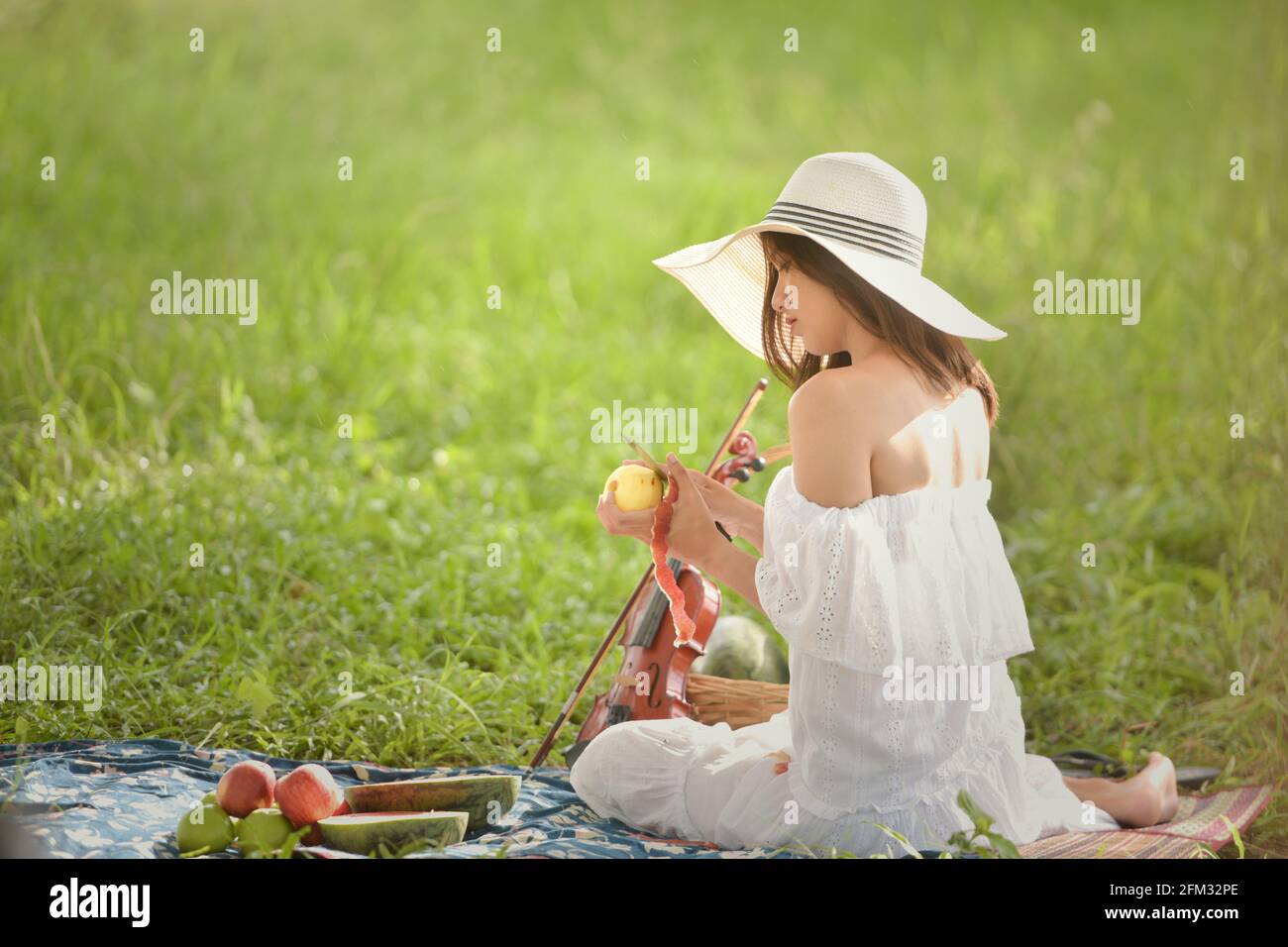 Woman sitting on a picnic blanket peeling an apple, Thailand Stock Photo