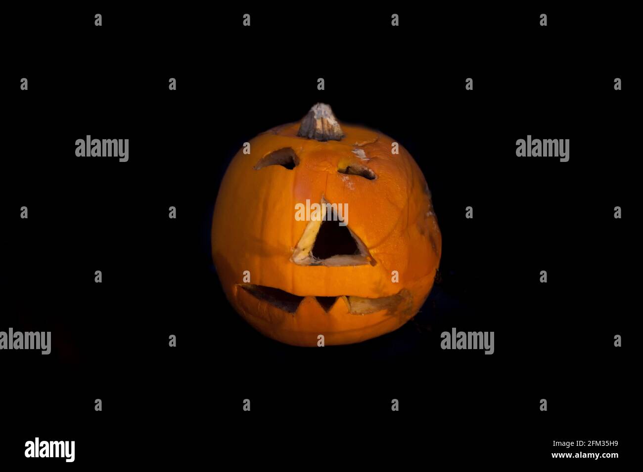 A decaying jack-o-lantern pumpkin with carved face caving in and rotting, on a black background Stock Photo