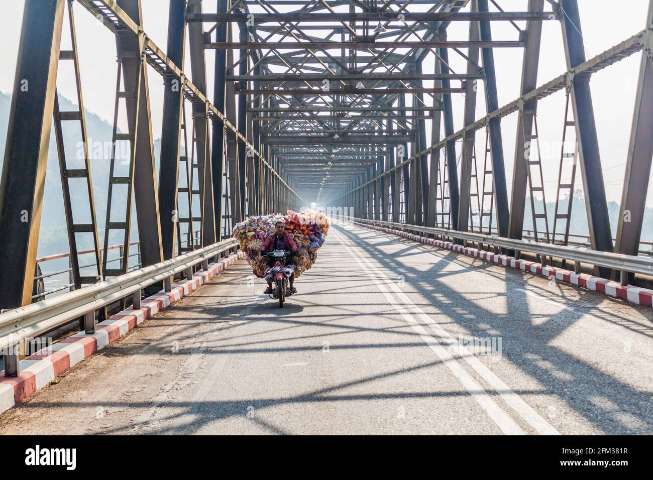 HPA AN, MYANMAR - DECEMBER 13, 2016: Local man on a heavily loaded motorbike crosses a bridge over Thanlwin Thanlyin river near Hpa An. Stock Photo