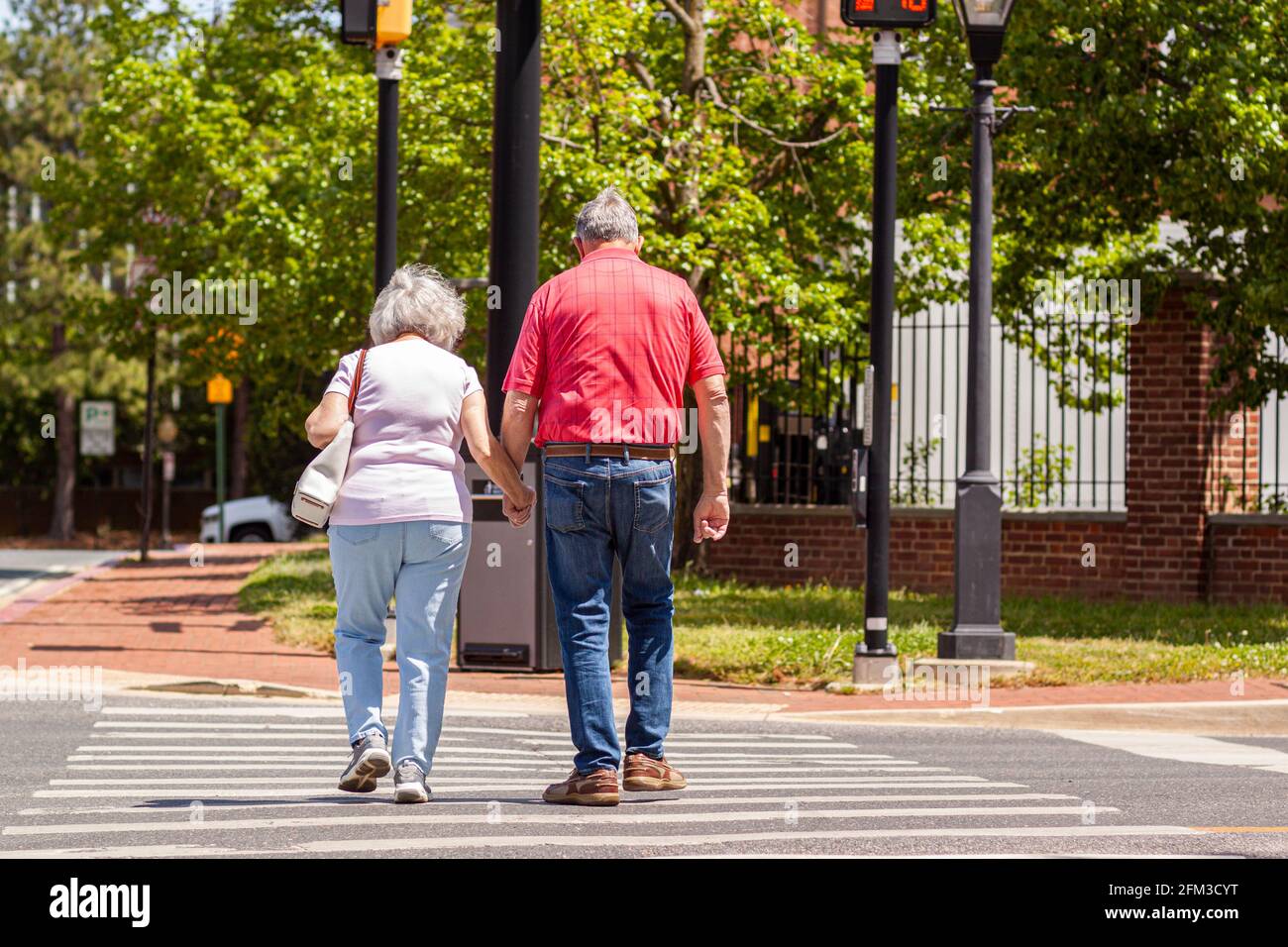 Senior caucasian couple in love holding hands as they cross the street on pedestrian crossing on a lovely spring day. Activity, togetherness at elderl Stock Photo