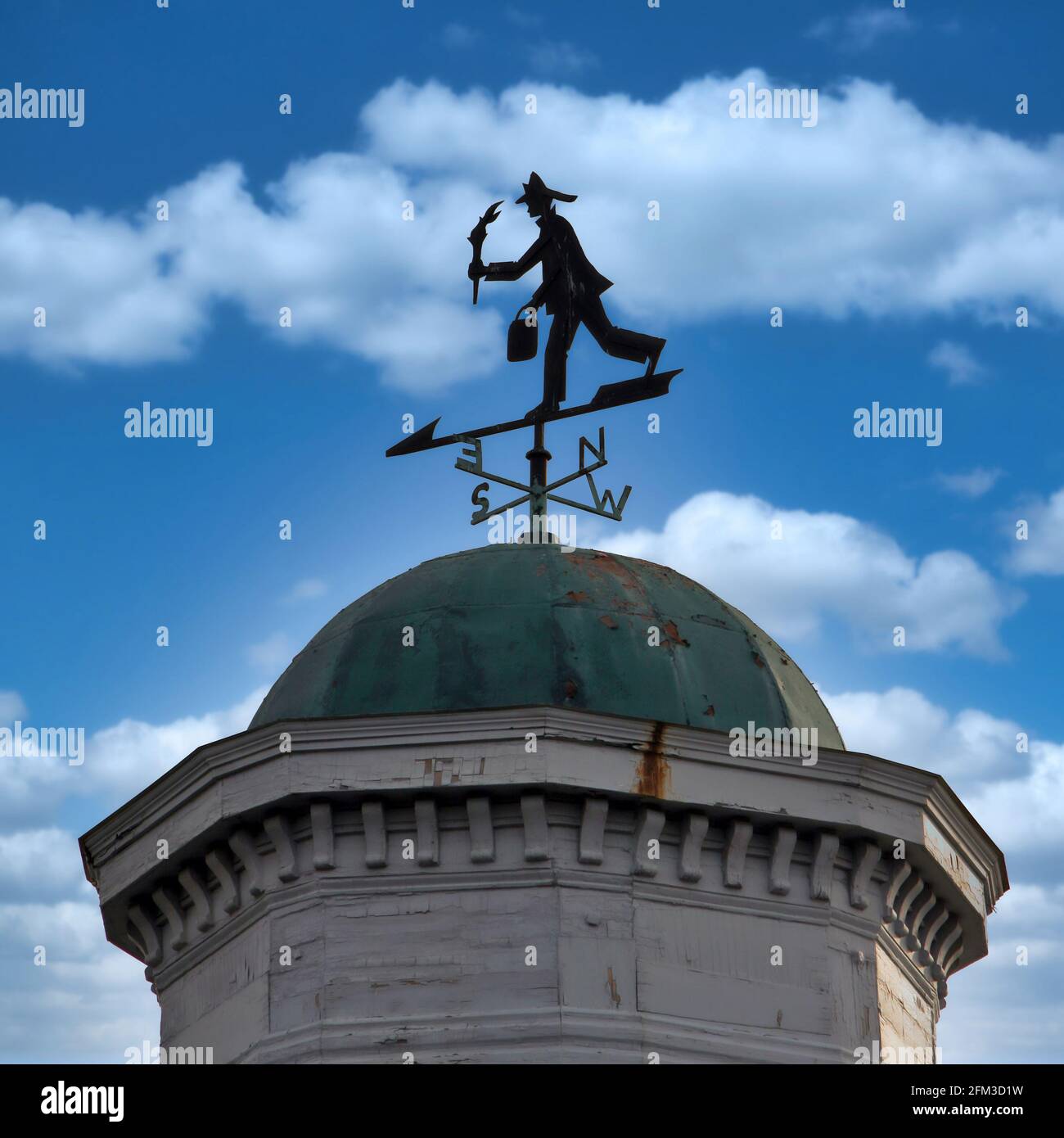 A fire fighter themed weather vane on a domed cupola of a building. Stock Photo