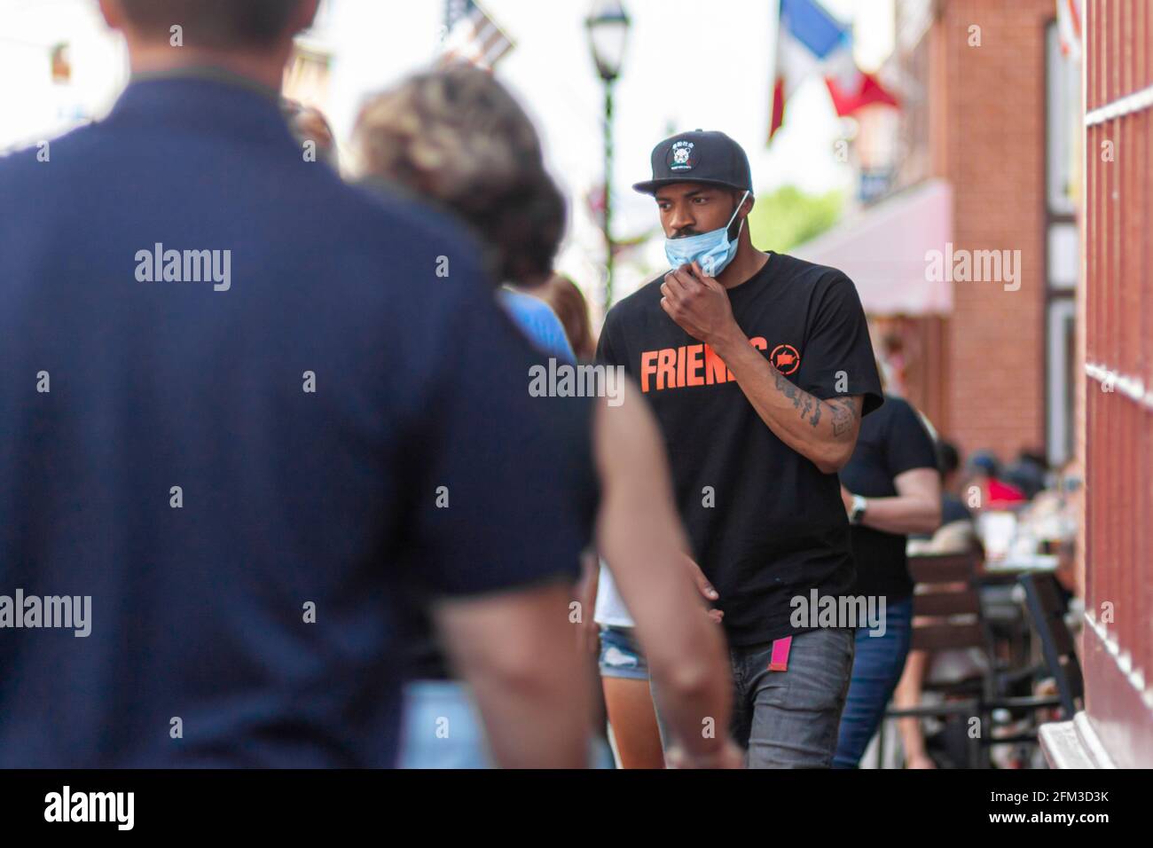 Annapolis, MD, USA 05-02-2021: A young African American man is removing his face mask in a crowded area in the street despite ongoing COVID-19 pandemi Stock Photo