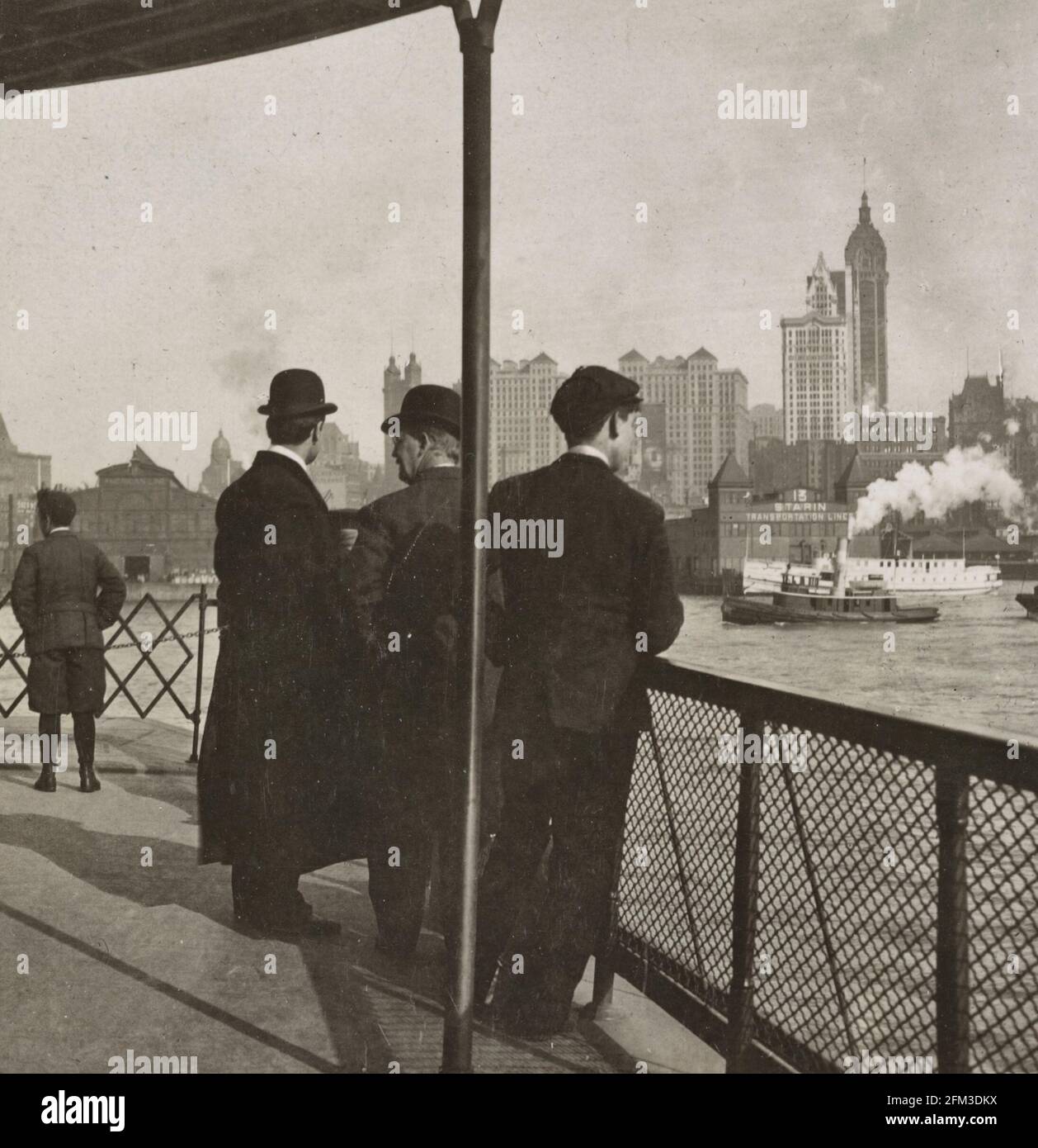 Singer Tower and huge office buildings, seen from ferry in North River, New York, USA - showing three men on ferry looking at boats and New York City in the distance, circa 1908 Stock Photo