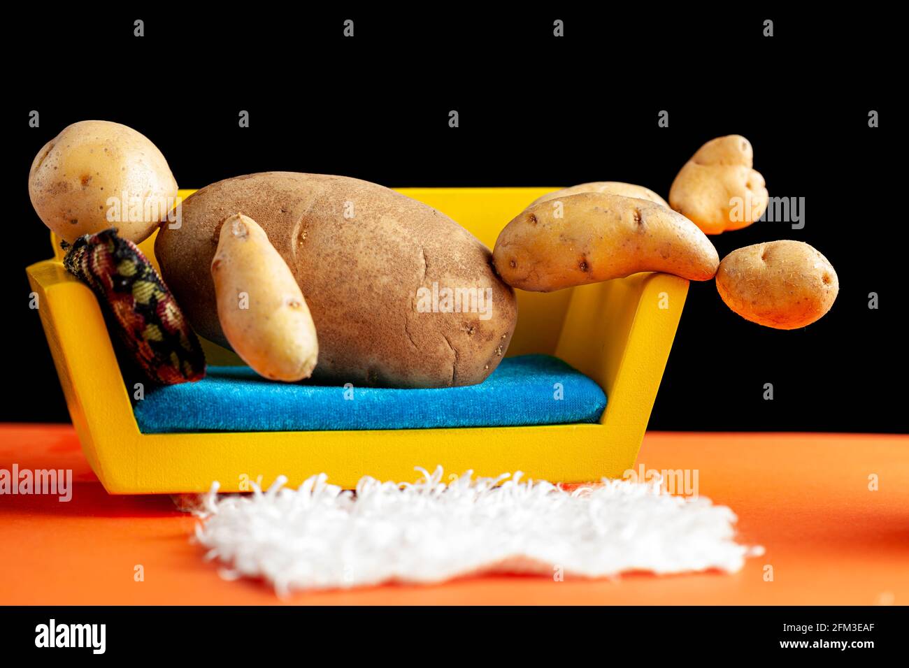 A quirky metaphorical concept image showing a potato man lying on a couch in a living room setting. Image for being couch potato, obesity, sedentary l Stock Photo