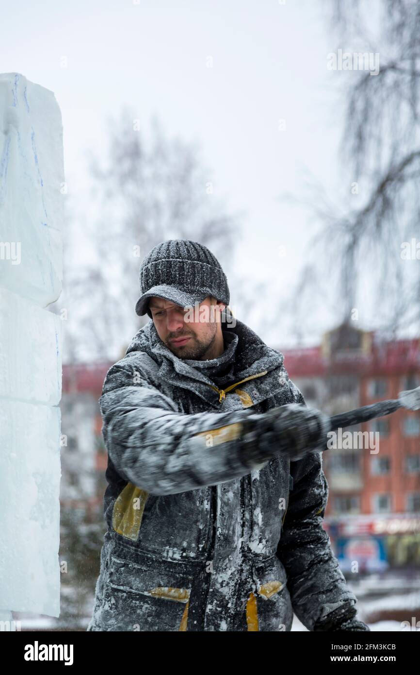 The sculptor beats off a piece of ice from an ice block with a chisel ...