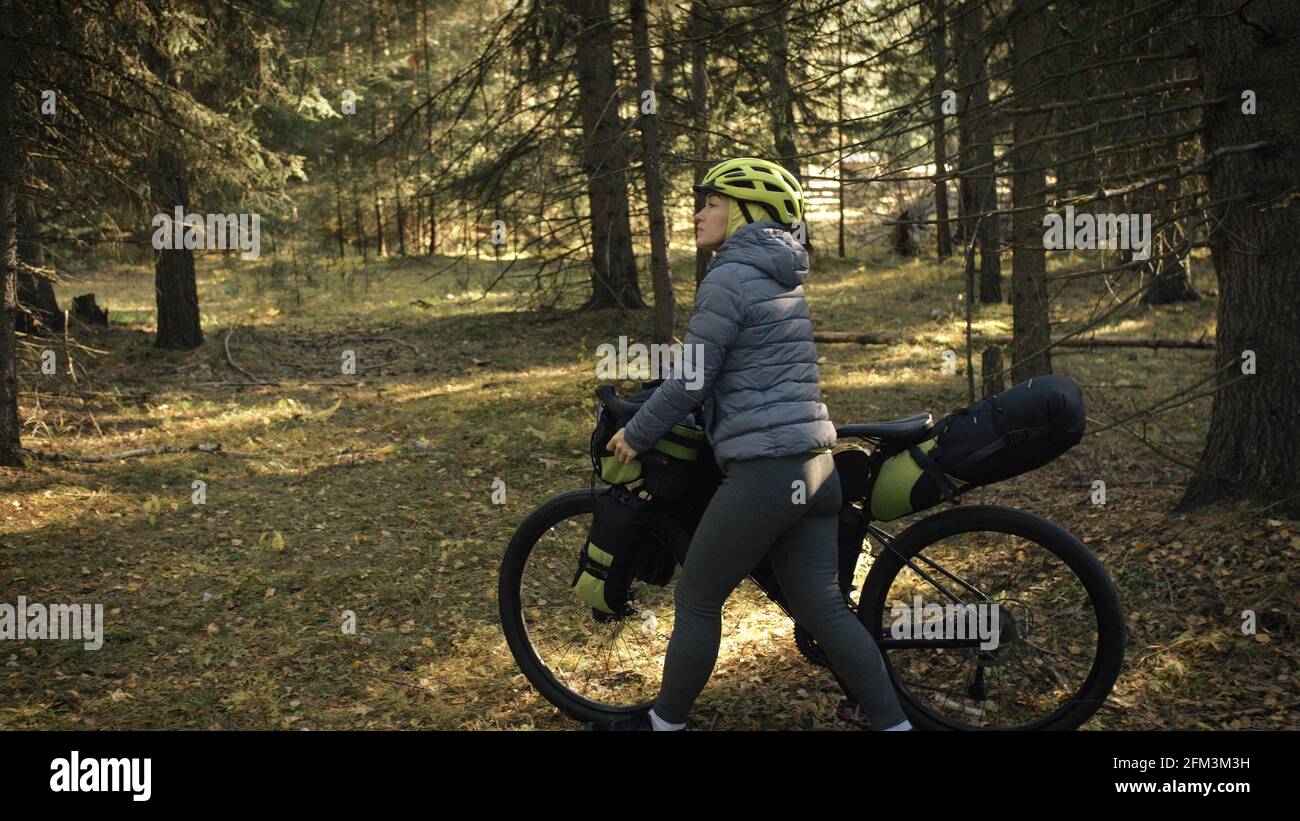 The woman travel on mixed terrain cycle touring with bike bikepacking. The traveler journey with bicycle bags. Magic forest park. Stock Photo