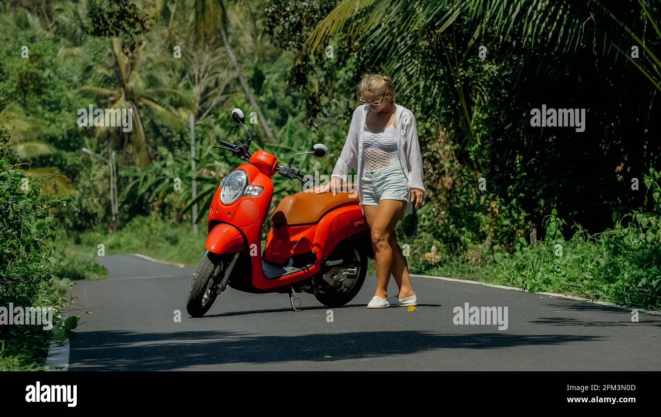 Woman on red scooter in white clothes drive on forest road trail. Dancing  trip. One girl caucasian tourist in sunglasses dance, relax near motorbike  Stock Photo - Alamy