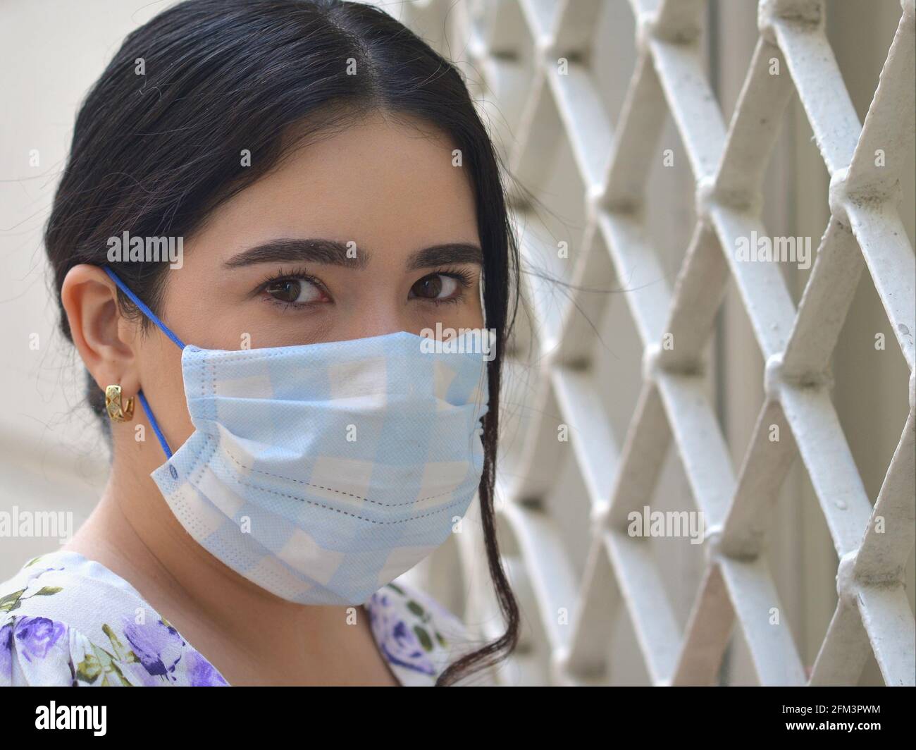 Young sexy Mexican girl with beautiful brown eyes wears a light-blue disposable surgical ear-loop face mask during the global coronavirus pandemic. Stock Photo