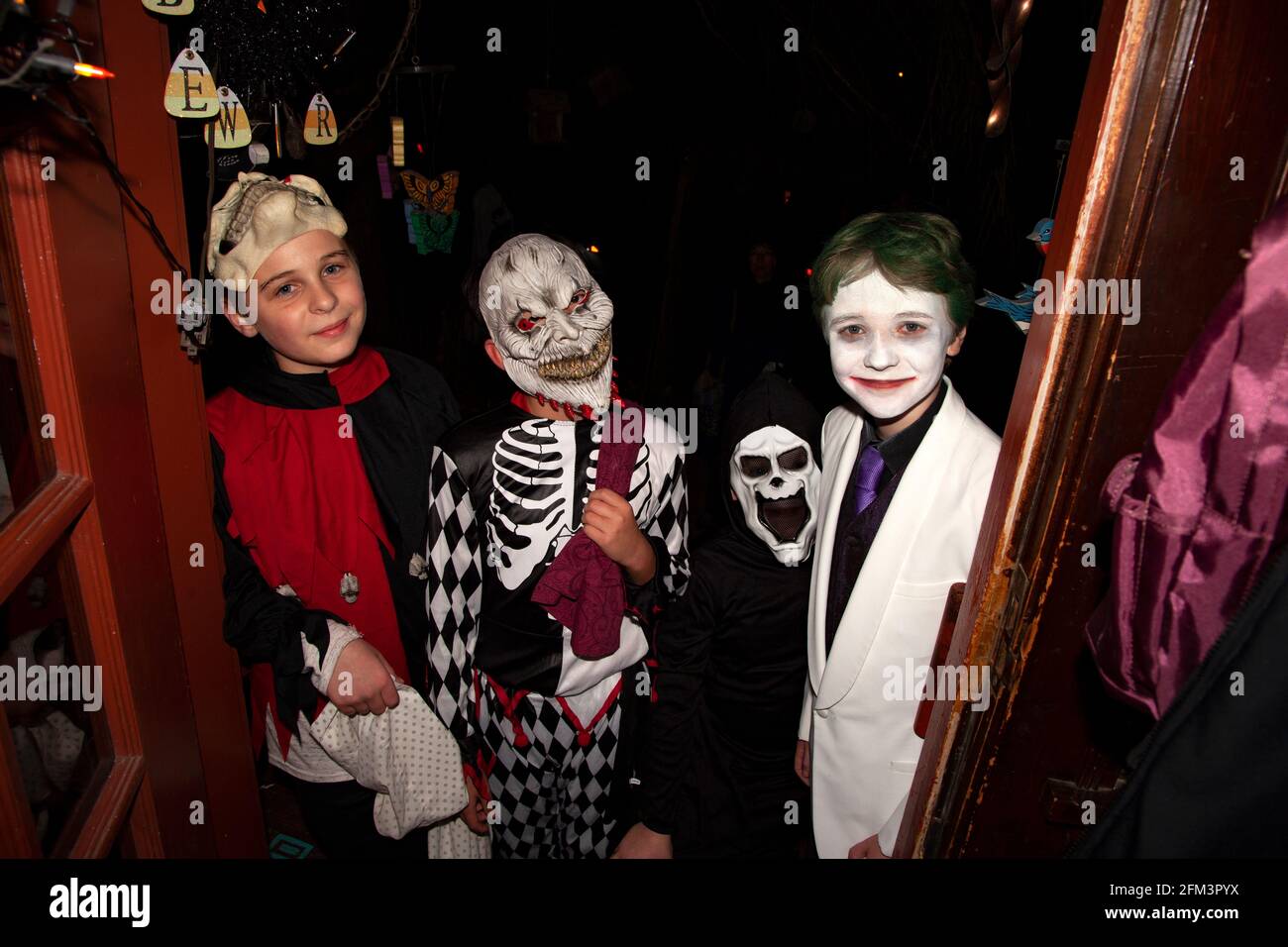 Halloween trick and treaters costumed as a skeleton, ghost, formal white jacketed, and jester. St Paul Minnesota MN USA Stock Photo
