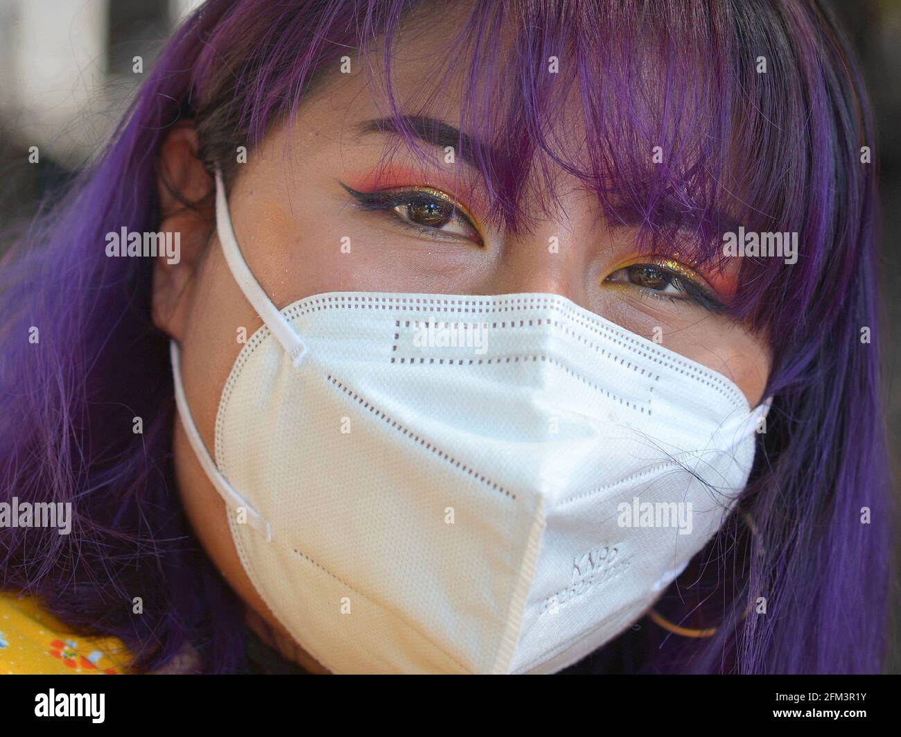 Young indigenous South American woman with elaborate beautiful eye make-up and blue dyed hair wears a KN95 face mask during the coronavirus pandemic. Stock Photo
