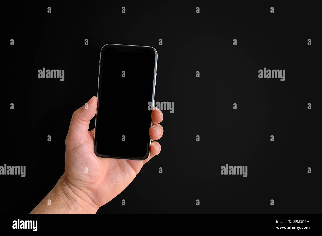Man holding mobile phone with blank screen on black background, closeup of hand. Space for text Stock Photo