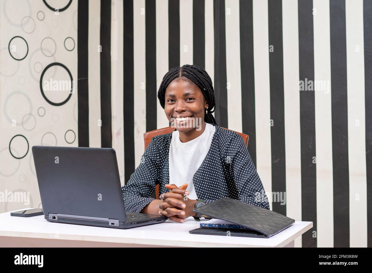 Happy African woman sitting by her desk and smiling at the camera after ...